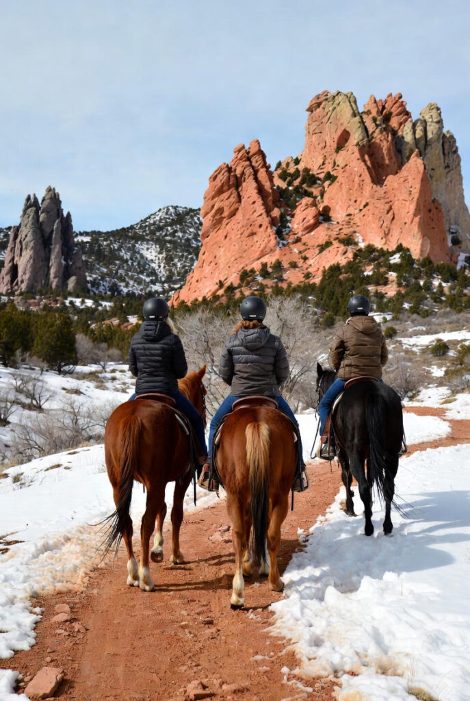 give me a photo of a group of three people horseback riding through Garden of the Gods in Colorado Springs in the winter - from the back